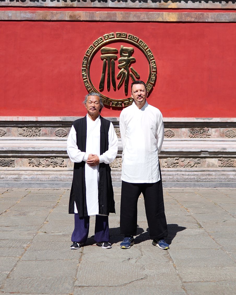 Mistrz Gu Shiyi i Maciej Marczak przed ścianą ze znakiem 祿 w Górach Wudang